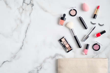 Makeup bag with cosmetic products spilling out on to marble table. Flat lay, top view. Glamor make up artist pouch with beauty productsの写真素材