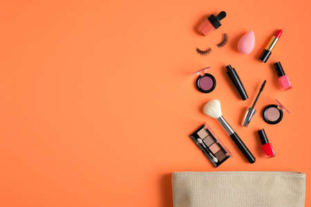 Makeup bag with cosmetic products spilling out on to pastel peach color background. Flat lay, view from above. Stylish make up artist pouch with beauty productsの写真素材