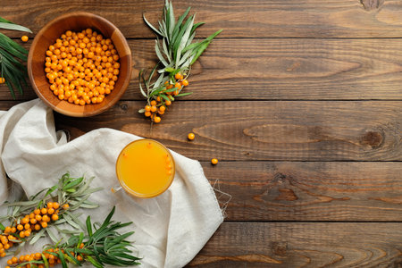 Sea buckthorn juice and sea buckthorn berries in bowl, plant branches on wooden table. Flat lay...