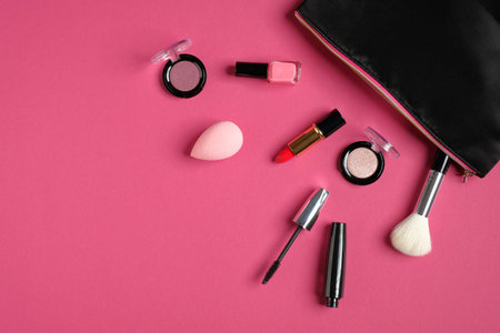 Makeup bag with cosmetic products spilling out on to pink background. Flat lay, top view. Glamor...