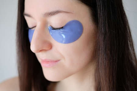 Young woman face with eye patches moisturizing skin under the eyes. Face skin care and beauty treatment concept. Closeup portrait.の写真素材