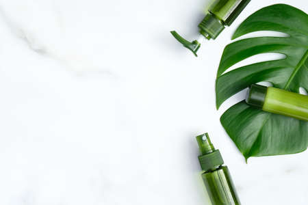 Flat lay natural organic cosmetic set with tropical monstera leaf on marble background. Top view green cosmetic bottles packaging. Skin care, body treatment conceptの写真素材