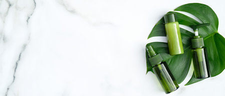 Green cosmetic bottles with monstera tropical plant leaves on marble background. Flat lay, top view,...