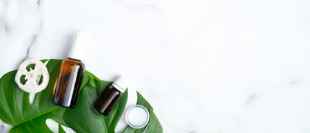 Essential oil bottles, loofah sponge and moisturizer cream with monstera tropical plant leaves on...