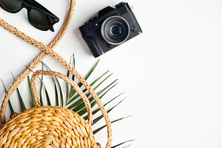 Flat lay stylish traveler accessories with tropical palm leaf branches on white background. Top view woven rattan straw bag, vintage camera, sunglasses. Travel vacation conceptの写真素材