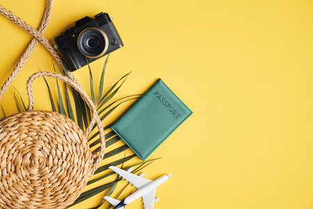 Flat lay traveler accessories on yellow background with rattan straw bag, plane model, tropical palm...