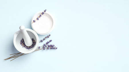 Natural face cream and mortar with lavender flowers on blue background. Organic SPA cosmetic product, skin care, body treatment concept. Flat lay, top viewの写真素材