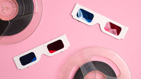Cardboard 3d glasses and reels of film on pink background. Watching movie at cinema concept.の写真素材
