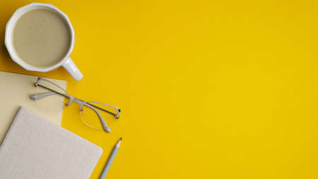 Modern office desk table with cup of coffee, glasses, notebook and pencil on yellow background. Top view with copy space, flat lay. Minimal style workspace design, stylish feminine workplace.の写真素材