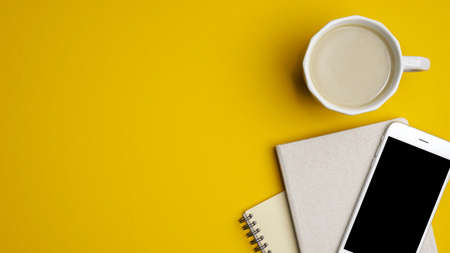 Modern office desk table with coffee cup, notebook, smartphone on yellow background. Minimal style hipster workspace. Top view with copy space, flat lay.の写真素材