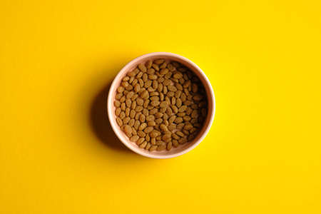 Bowl of dry kibble cat food on yellow background top view. Pet care concept.の写真素材
