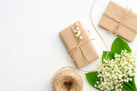 Present or gift boxes wrapped kraft paper, flowers lily of the valley and twine rope on white table. Flat lay, top view. Wedding, Mother's Day or Women's Day concept.の写真素材