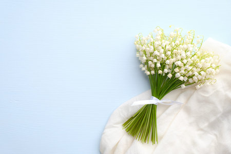Bouquet of flowers lily of the valley and cloth on blue background with copy space. Mothers or Womens Day greeting card template, wedding invitation mockup.の写真素材