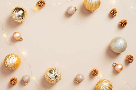 Minimal Christmas composition. Christmas frame border made of golden balls, cones, garland on pastel beige background. Glamor, fashion style. Flat lay.の写真素材