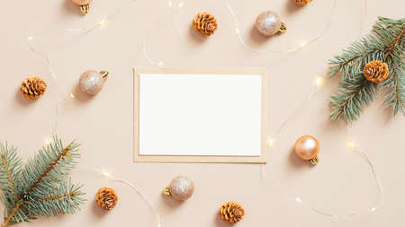 Christmas letter envelope with blank paper card, golden decorations, pine tree branches and cones on pastel beige background. Flat lay, top view.の写真素材