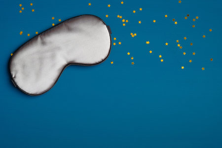 Gray sleep eye mask on dark blue background with confetti. Sleep healthy, good night, insomnia treatment conceptの写真素材