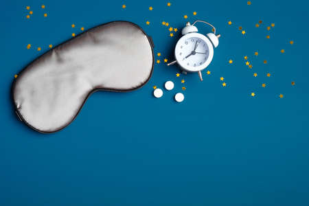 Insomnia treatment concept. Flat lay composition with sleep eye mask, alarm clock and sleeping pills.の写真素材