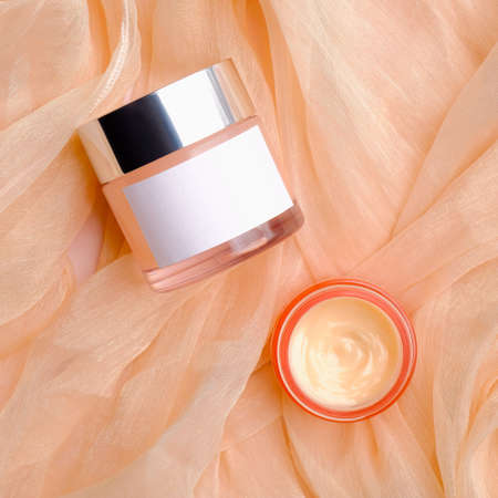 Cosmetic product packaging design, face cream jar mockup with white label and moisturizer lotion on beige silky fabric. Flat lay, top view.の写真素材