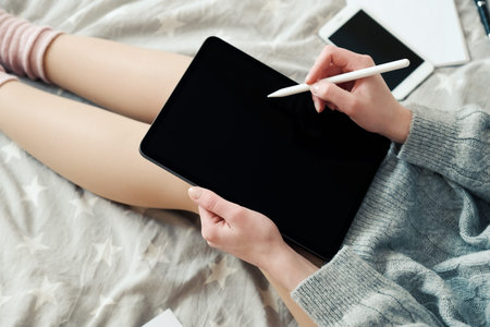 Young female freelancer graphic designer working with drawing digital tablet in bed at home,...