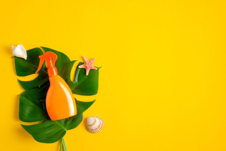 Sunscreen spray bottle and tropical leaves on yellow background. Flat lay, top view. Sun protection,...