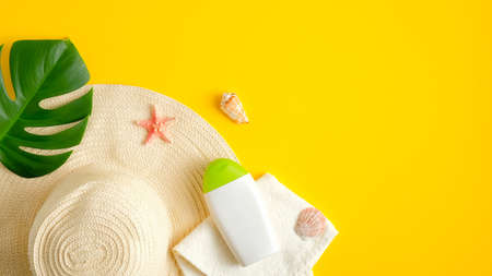 Sunscreen cream lotion bottle, beach hat and tropical leaves on yellow background. Summer sun protection concept. Flat lay, top viewの写真素材