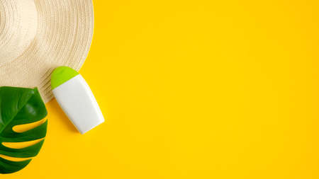 Suntan lotion bottle on yellow background with female beach hat and tropical leaf. Top view with copy space. Sun protection cosmetic products, summer skin care conceptの写真素材