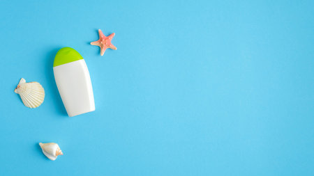 Blank suntan cream bottle and seashell on blue background. Sun protection on summer vacation concept