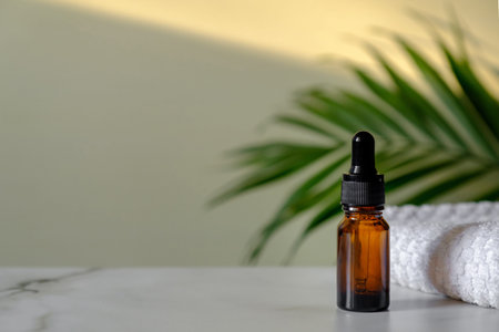 Essential oil bottle and towel on marble table, tropical palm leaf on background. Dropper bottle...