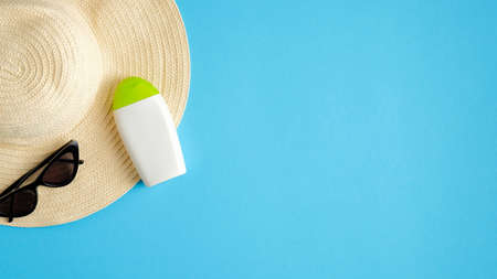 White sunscreen cream bottle without labels, sunglasses and beach hat on blue background. Top view with copy space. Summer make-up and skin care products conceptの写真素材