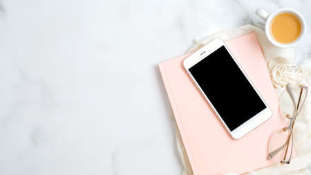 Home office desk table with pink paper notepad, smartphone screen mockup, women's glasses on marble background. Elegant feminine workspace with stylish accessories. Flat lay, top view.の写真素材