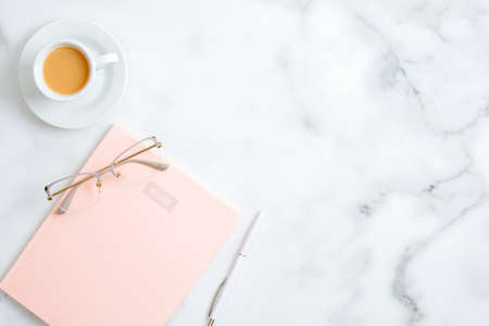 Flat lay home office desk. Female workspace with pink paper notebook, glasses, cup of coffee, pen on marble table. Top view feminine background with copy spaceの写真素材