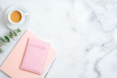 Home office desk workspace with pink paper notebook, pen, passport, cup of coffee on marble background. Flat lay, top view. Elegant feminine workplace with stylish accessoriesの写真素材