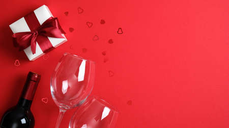 Romantic dinner table setting for Valentine's day. Bottle of wine, glasses, valentine gift on red background. Top view with copy spaceの写真素材