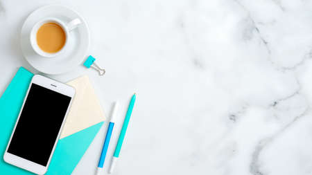 Flat lay feminine home office desk with smartphone empty screen mockup, mint notebook, stationery, stylish accessories, coffee cup on marble background. Top view with copy space.の写真素材
