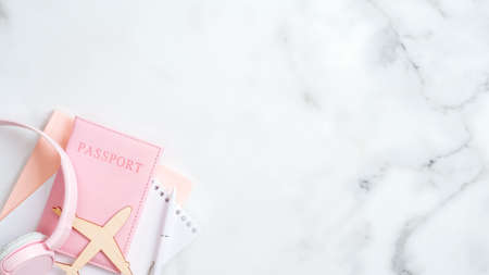 Summer vacation and travel concept. Flat lay design with airplane, pink passport, paper notepad, headphones on marble background. Top view with copy space.の写真素材