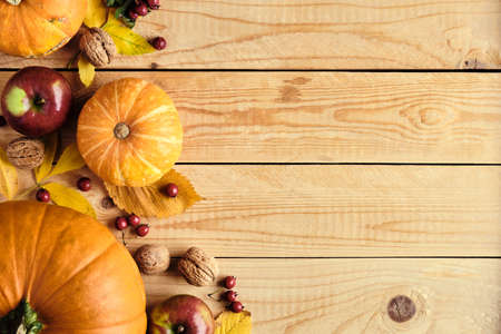 Autumn holiday concept with pumpkins, fallen leaves, nuts, red berries on wooden table. Thanksgiving background. Flat lay, top view, copy space.の写真素材