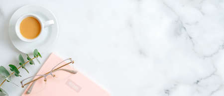 Pink paper notepad, women's glasses, cup of coffee, eucalyptus leaf on marble background with copy space. Beauty blog banner mockupの写真素材