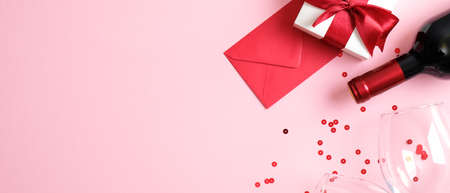 Valentine's day romantic dinner concept. Top view table setting with bottle of wine champagne, two glasses, gift box, envelope with love letter and confetti on pink background. Flat lay, top viewの写真素材
