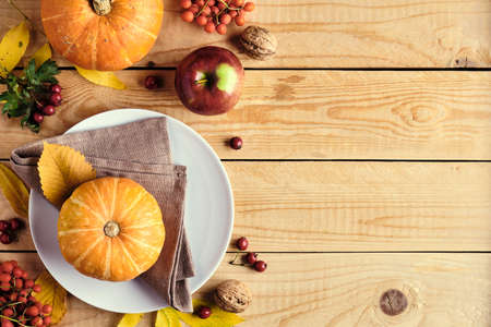 Happy Thanksgiving holiday background. Pumpkins, fallen leaves, plate, apples, red berries on wooden table. Thanksgiving dinner concept. Flat lay, top view, copy space.の写真素材