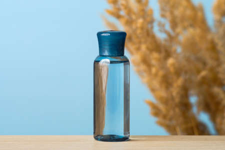 Transparent blue cosmetic bottle with water based moisturizing lotion on blue background with dry flowers. Clear plastic bottle, beauty product packaging design, cosmetic package brandingの写真素材