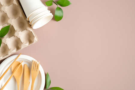 Eco-friendly kitchen tableware set concept. Flat lay egg box, wooden cutlery, paper cups and plate, green leaves. Top view with copy space. Zero waste, plastic free concept. Sustainable lifestyle.の写真素材