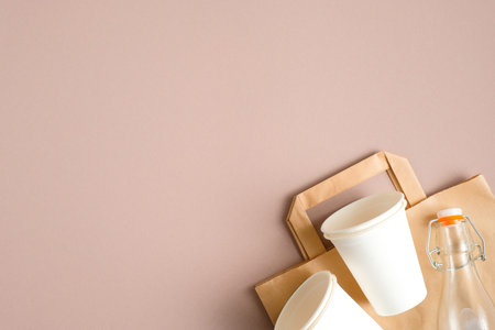 Biodegradable paper bag, eco-friendly drinking cups and glass bottle on brown background. Flat lay,...