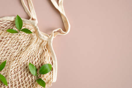 Reusable grocery mesh bag with green leaves on brown background. Organic cotton shopping bag concept. Flat lay, top view.の写真素材