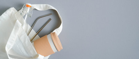 Reusable bamboo coffee cup, glass bottle and stainless steel drinking straws in cotton shopping bag. Eco-friendly drinking cutlery set, top view. Zero waste eco shop banner designの写真素材