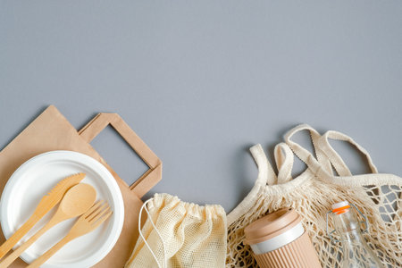 Eco-friendly cutlery set, grocery bags, bamboo coffee cup, glass bottle on gray background. Zero...