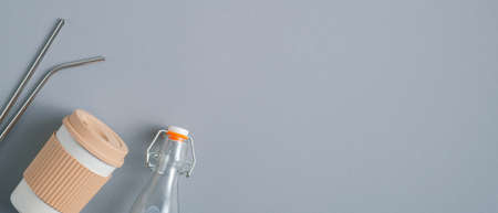 Zero waste concept. Reusable bamboo coffee cup, Glass bottle, stainless steel drinking straws on gray background. Eco shop banner designの写真素材