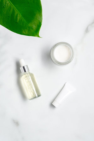 Natural organic cosmetics set. Serum lotion in glass dropper bottle, moisturizer, tube with cream on marble table. Flat lay, top view.