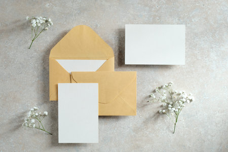 Blank paper cards, envelopes with flowers on a concrete table.