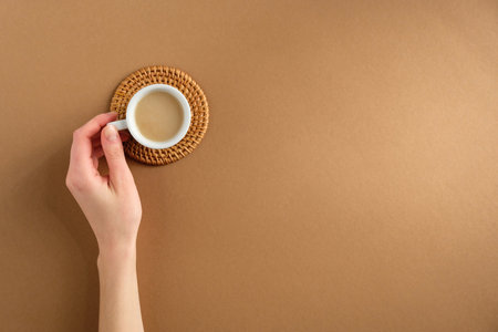 Woman's hand holding cup of coffee on brown background. Flat lay, top view.の写真素材