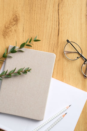 Elegant freelancer workspace with paper notebook, diary, glasses, eucalyptus leaves on wooden table. Home office desk. Top view, flat layの写真素材